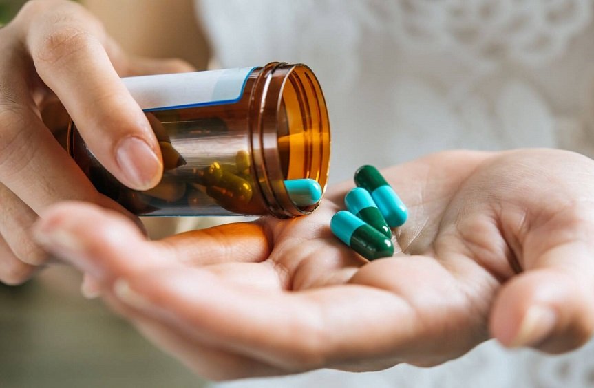 A imagem mostra uma mão segurando vários comprimidos de antibióticos, simbolizando a preocupação com o uso incorreto destes medicamentos.