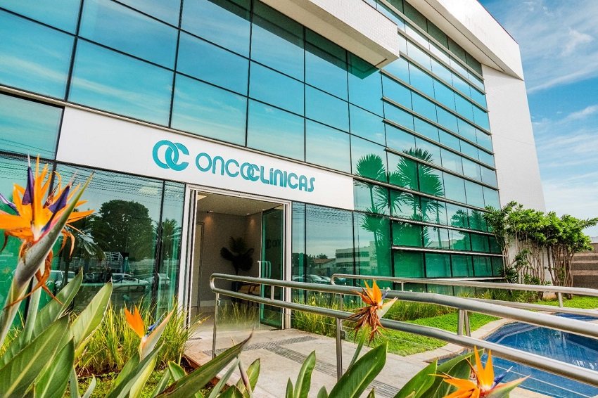 Logotipo da Oncoclínicas&Co com a bandeira do Brasil ao fundo